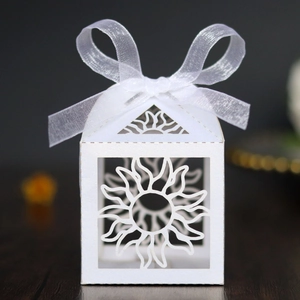 Detail of white laser-cut hollow sun pattern candy box with a delicate white silk ribbon