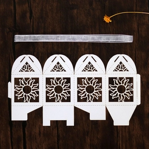 Flat lay of laser-cut sunflower paper gift box template with silver ribbon on wood