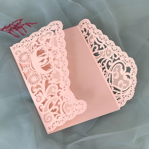 Close-up of pink laser-cut wedding invitation with lace patterns and pumpkin carriage