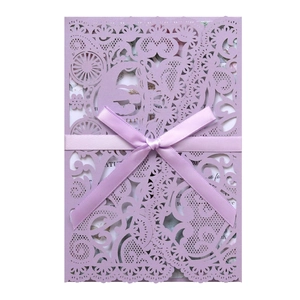 Detail of purple laser-cut wedding invitation with elegant silk bow and floral insert