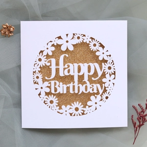 Macro shot of laser-cut daisy wreath and golden glitter Happy Birthday card on mesh fabric