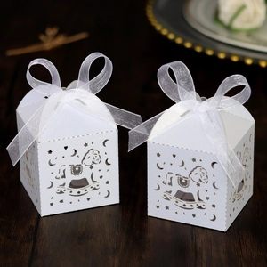 Detailed laser-cut white favor boxes with rocking horse patterns and organza ribbon