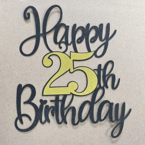 Macro shot of glittery black and gold Happy 25th Birthday cake topper with laser cut detail