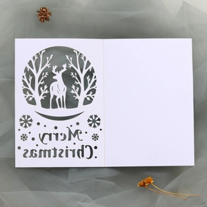 Close-up of laser-cut Merry Christmas card featuring forest reindeer and snowflakes