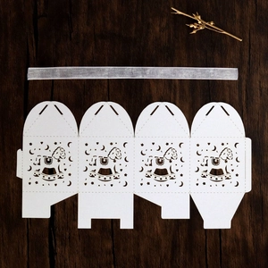 Flat lay of white laser-cut rocking horse candy boxes with silver ribbons on wood