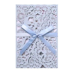 Detail of laser-cut light blue wedding invitation with silk bow and floral liner