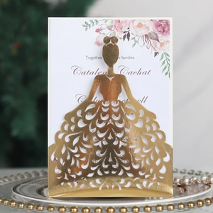 Close-up of gold laser-cut dress-shaped wedding invitation on ceramic plate with pearls