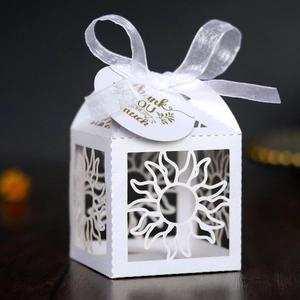 Close-up of laser-cut sun pattern on white gift box with silk ribbon and thank you tag