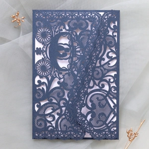 Detail of laser-cut navy wedding invitation featuring intricate floral and pumpkin coach patterns