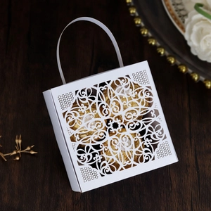 Detail of white laser-cut lace candy box with gold foil chocolates on wooden background