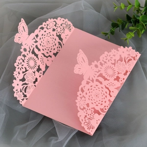 Macro shot of laser-cut pink wedding invitation card featuring floral and butterfly details