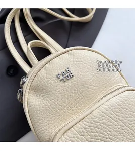Détail du mini sac à dos crème en cuir grainé avec logo métallique et fermetures éclair