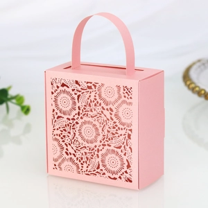 Detail of light pink laser-cut wedding candy box with floral hollow pattern and handle