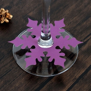 Close-up of purple snowflake wine glass escort card with cutout design on dark wood