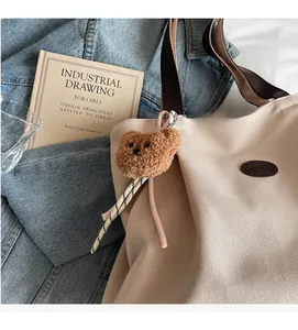 Gros plan d'un sac cabas en toile crème avec bandoulière marron et charm ours en peluche