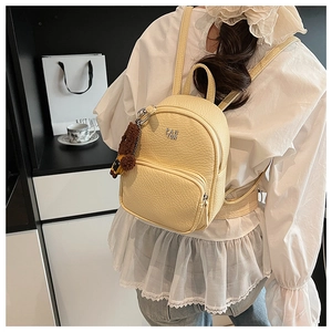 Gros plan d'un sac à dos crème en similicuir avec charme d'ours en peluche et logo