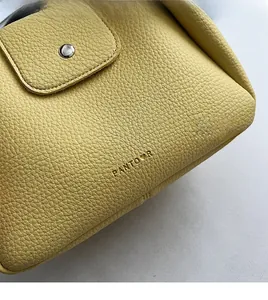 Detail of yellow lychee grain leather handbag featuring silver snap and logo
