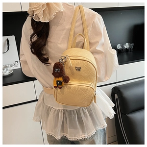 Détail d'un mini sac à dos jaune avec texture cuir et petit pendentif chien mignon