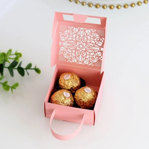 Detailed laser-cut pattern on light pink wedding favor box with an elegant handle