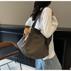 Détail d'un grand sac cabas en toile marron avec anses en cuir et breloque petit ours