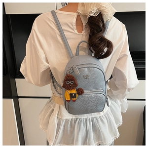 Gros plan du sac à dos bleu clair motif litchi avec une breloque en peluche de caniche