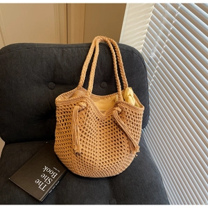 Détail d'un sac cabas en paille tressée à la main avec pompon et design évidé sur chaise