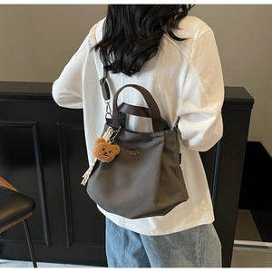 Détail d'un sac fourre-tout en toile marron avec anses en cuir et pendentif ours