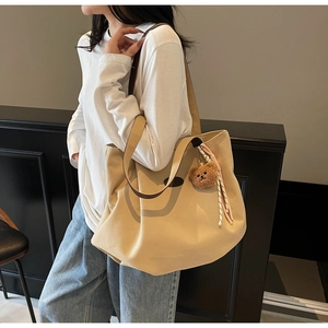 Vue portée d'un grand sac cabas en toile beige avec anses brunes et breloque ours peluche
