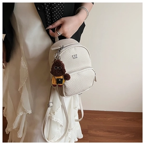 Gros plan d'un mini sac à dos crème avec texture litchi et un pendentif chien en peluche
