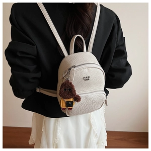 Détail du mini sac à dos en cuir blanc cassé avec un porte-clé chien en peluche mignon