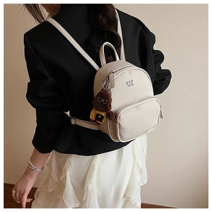 Détail d'un mini sac à dos crème texturé avec breloque ours en peluche porté par un mannequin