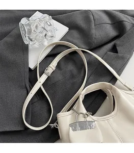 Detail of a creamy white leather handbag with adjustable strap and silver metal lock charm