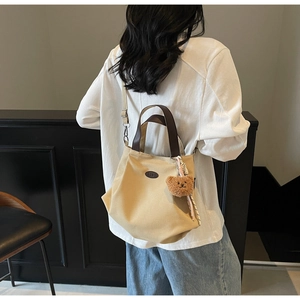 Vue détaillée du sac cabas en toile avec lanières en cuir et breloque ours sur tenue décontractée
