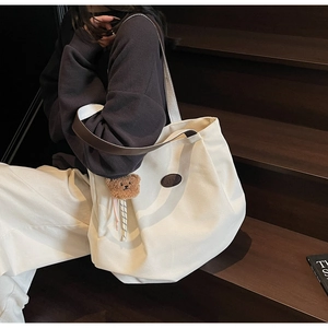Détail d'un sac cabas en toile blanche avec breloque ours sur un escalier en bois