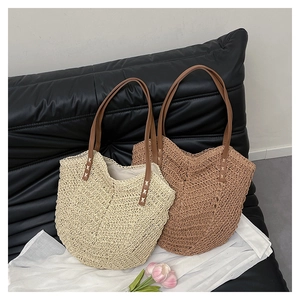 Close-up of woven straw tote bag details with leather handles and cross-stitch accents