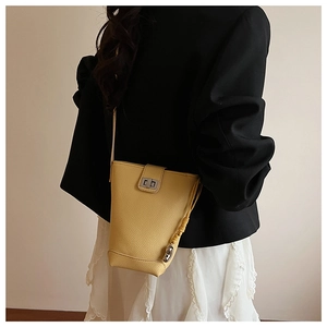 Close-up of light yellow bucket bag in pebble leather with metallic twist lock on a model