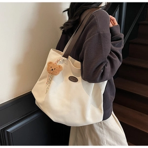 Détail d'un grand sac fourre-tout en toile blanc avec anses brunes et breloque ours