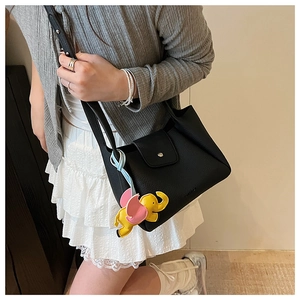 Detail of black litchi grain leather tote bag with a colorful elephant charm accessory