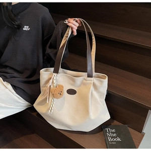 Détail du sac cabas en toile avec sangles en cuir et breloque ours sur marches en bois