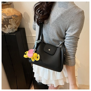 Close-up of black litchi grain leather bucket bag with a yellow elephant charm