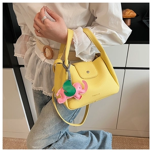 Close-up of yellow pebbled leather bucket bag with pink elephant charm and shoulder strap