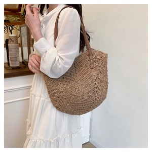 Detail of hand-woven straw tote bag with brown leather handles and reinforced stitching