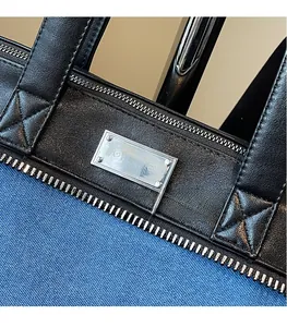 Detail of blue denim tote bag with black leather trim and silver metal logo plate