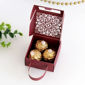Detail of laser-cut burgundy wedding favor box with lace pattern and golden chocolates