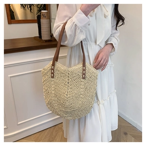 Detail of beige straw tote bag with brown leather handles and woven texture on model