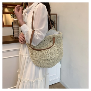 Detail of hand-woven straw tote bag featuring brown leather shoulder straps for beach trips
