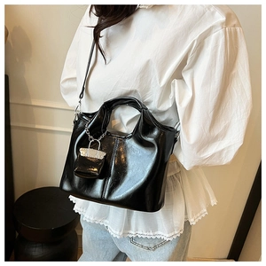 Detail view of a black glossy patent leather handbag with silver chain and chic dumpling shape