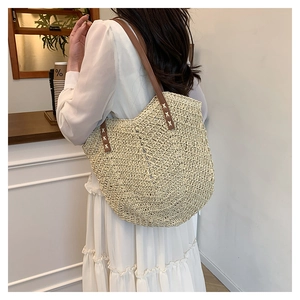 Detail of handwoven straw tote bag with brown leather shoulder strap and cross-stitch