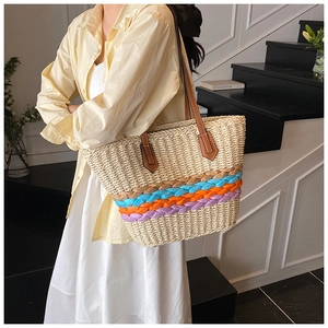 Detail of woven straw tote bag with colorful stripes and brown leather strap on model