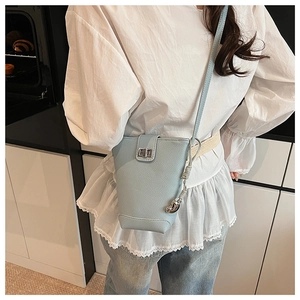 Light blue crossbody bucket bag with silver heart pendant on a model in white top